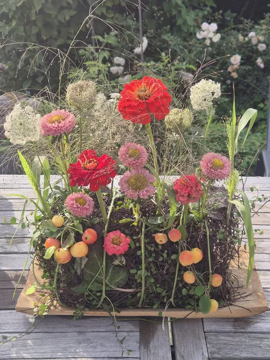 Een tafelschikking met zinnia's en sierappeltjes, een bezemsteel met gedroogde bloemen en rozenbottels, en een stuk voor Allerheiligen met rozen en asters